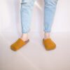 A woman wearing house slippers made of curcuma yellow and grayish brown wool felt