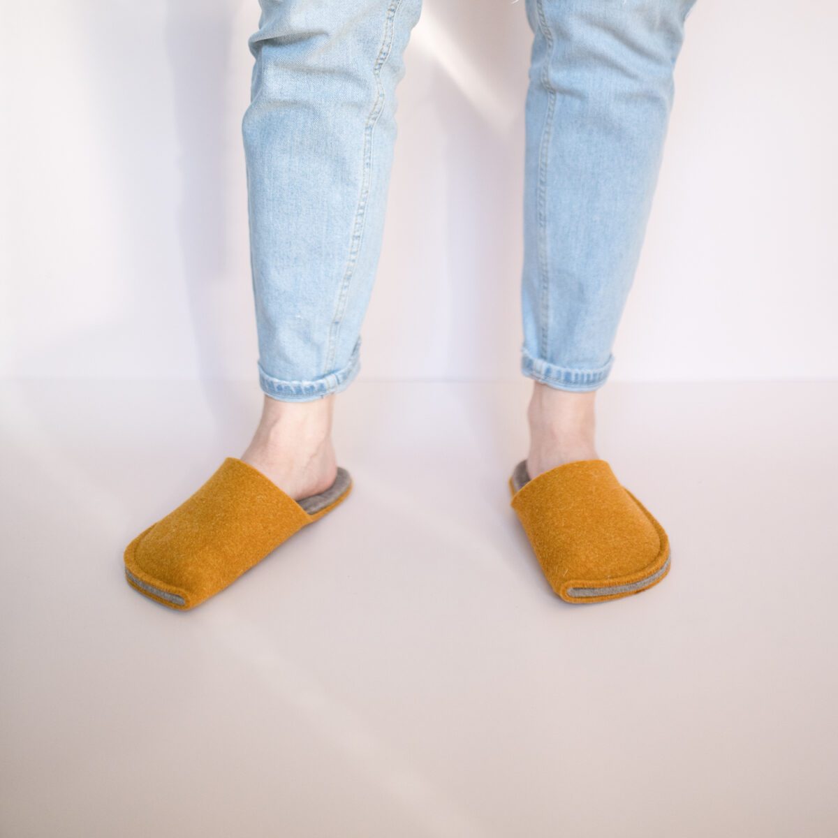 A woman wearing house slippers made of curcuma yellow and grayish brown wool felt