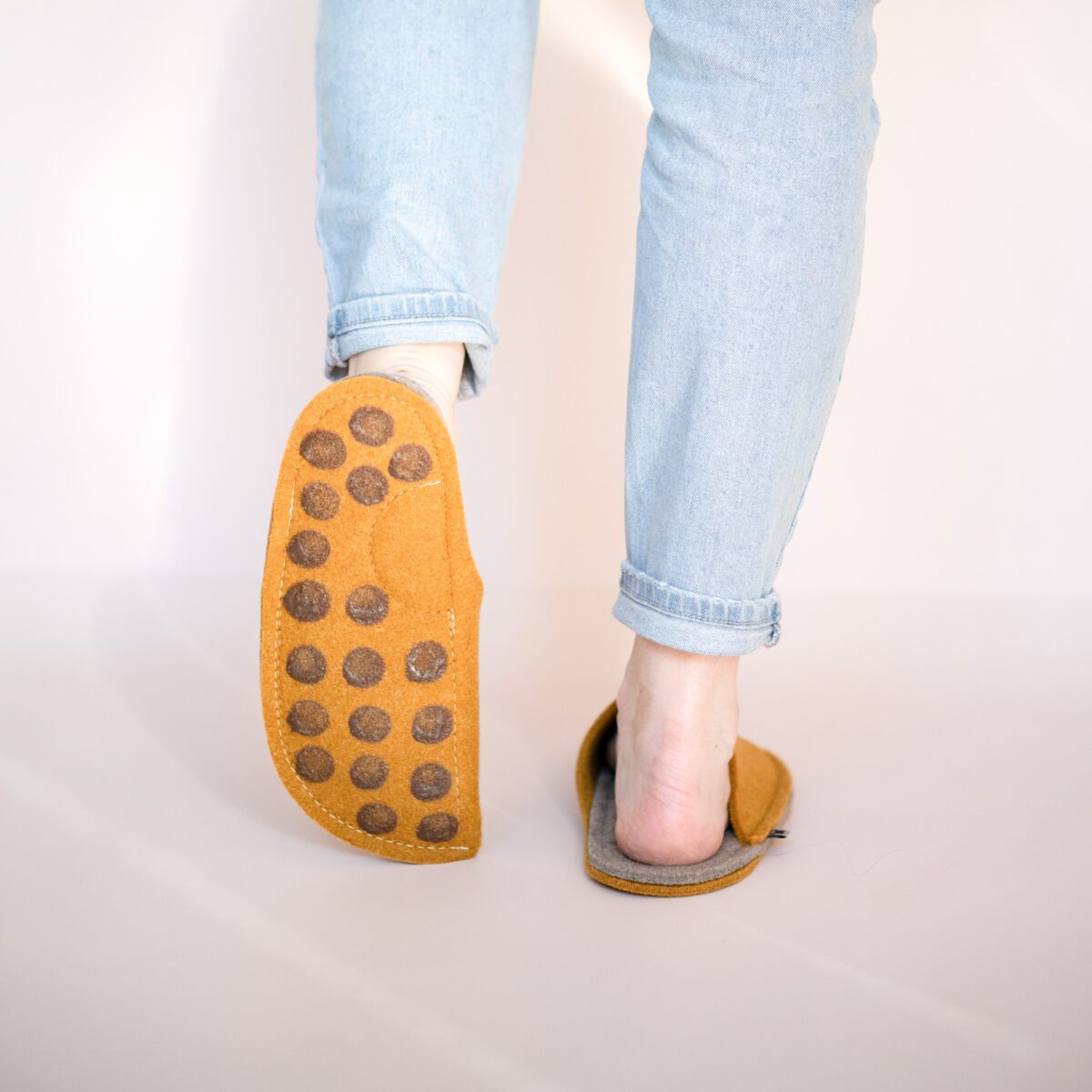 A woman wearing house slippers made of curcuma yellow and grayish brown wool felt