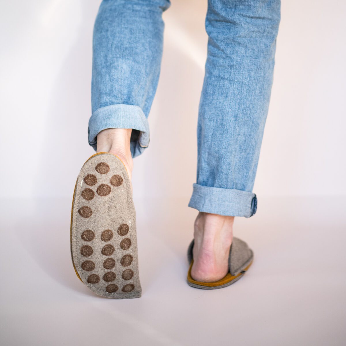 A man wearing house slippers made of curcuma yellow and grayish brown wool felt