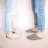 A couple wearing house slippers made of cream white and grayish brown wool felt