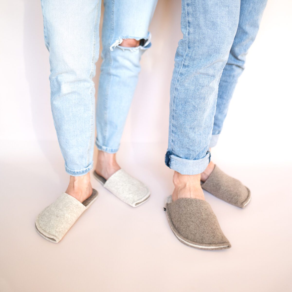 A couple wearing house slippers made of cream white and grayish brown wool felt