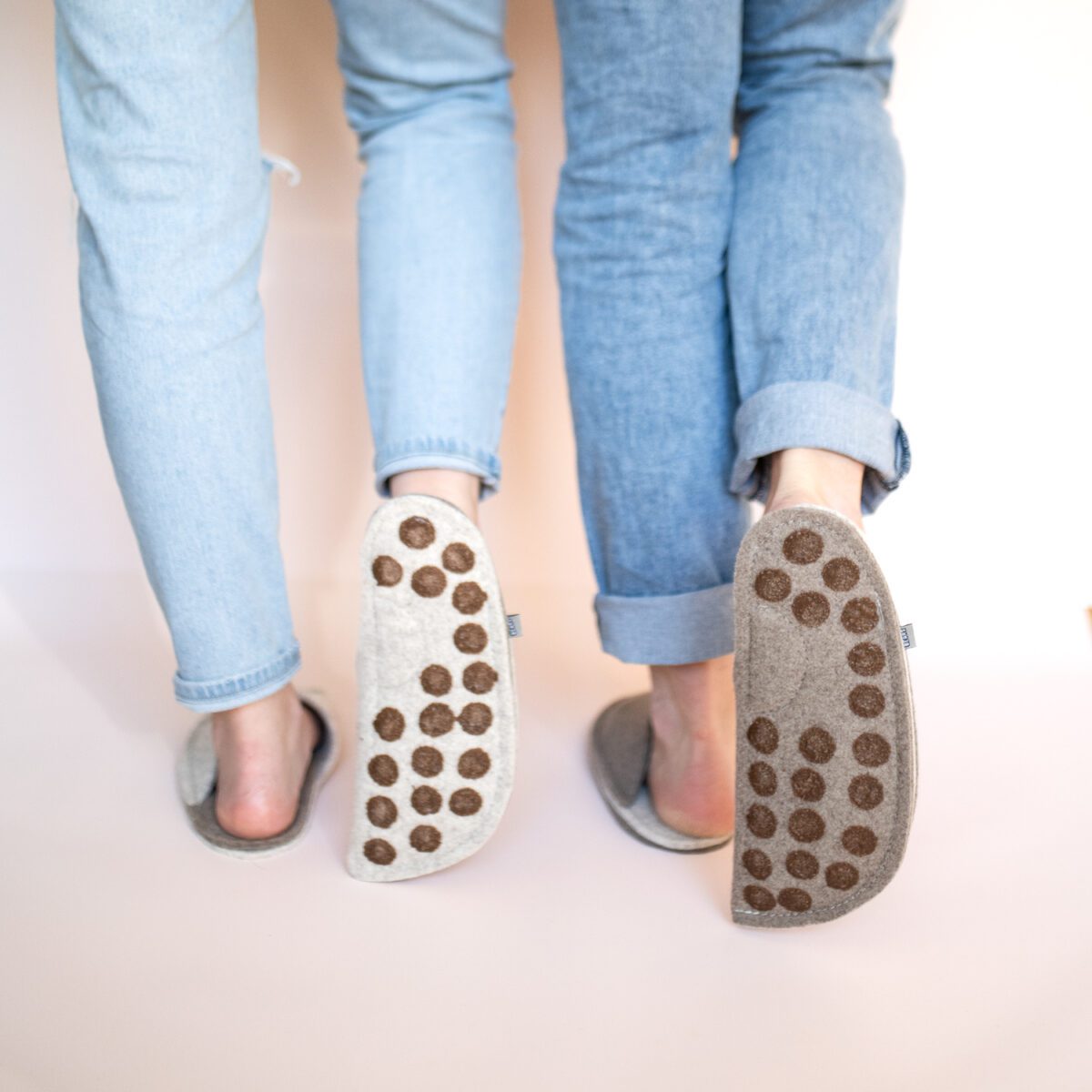 A couple wearing house slippers made of cream white and grayish brown wool felt