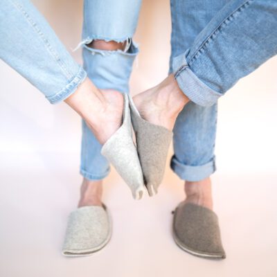 A couple wearing house slippers made of cream white and grayish brown wool felt