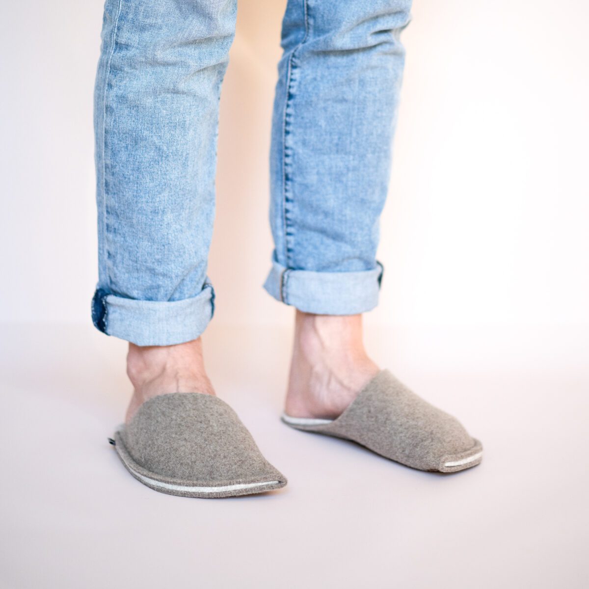 A man wearing house slippers made of cream white and grayish brown wool felt