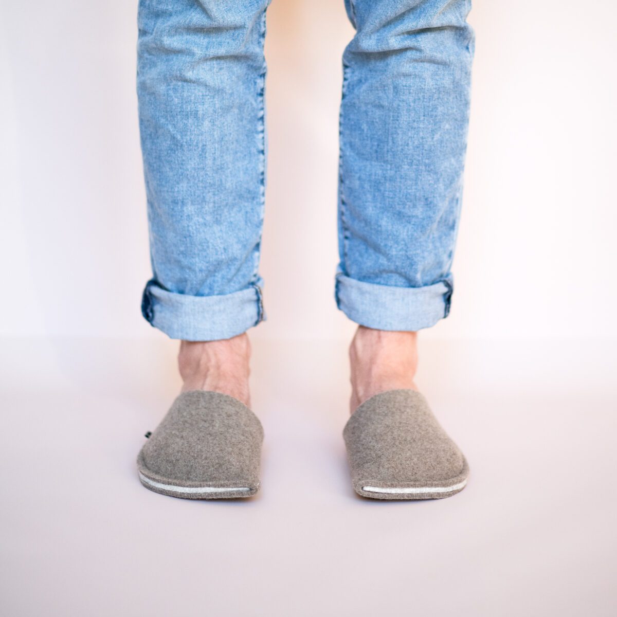 A man wearing house slippers made of cream white and grayish brown wool felt