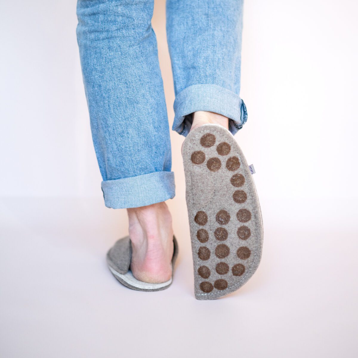 A man wearing house slippers made of cream white and grayish brown wool felt