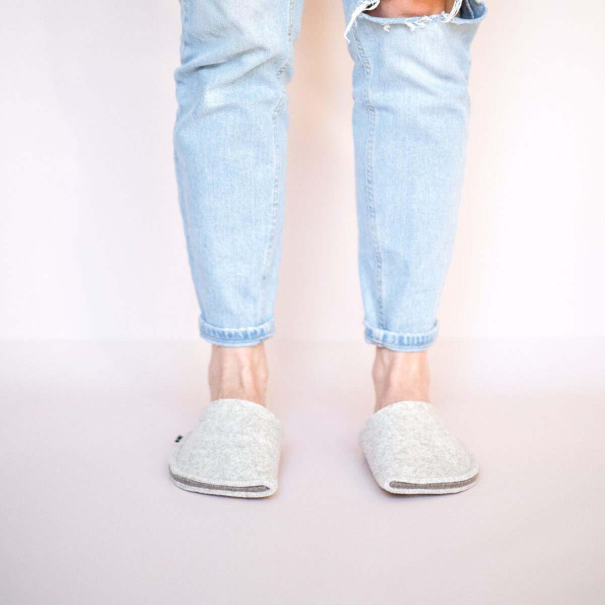 A woman wearing house slippers made of cream white and grayish brown wool felt