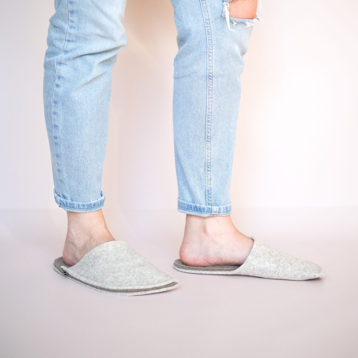 A woman wearing house slippers made of cream white and grayish brown wool felt