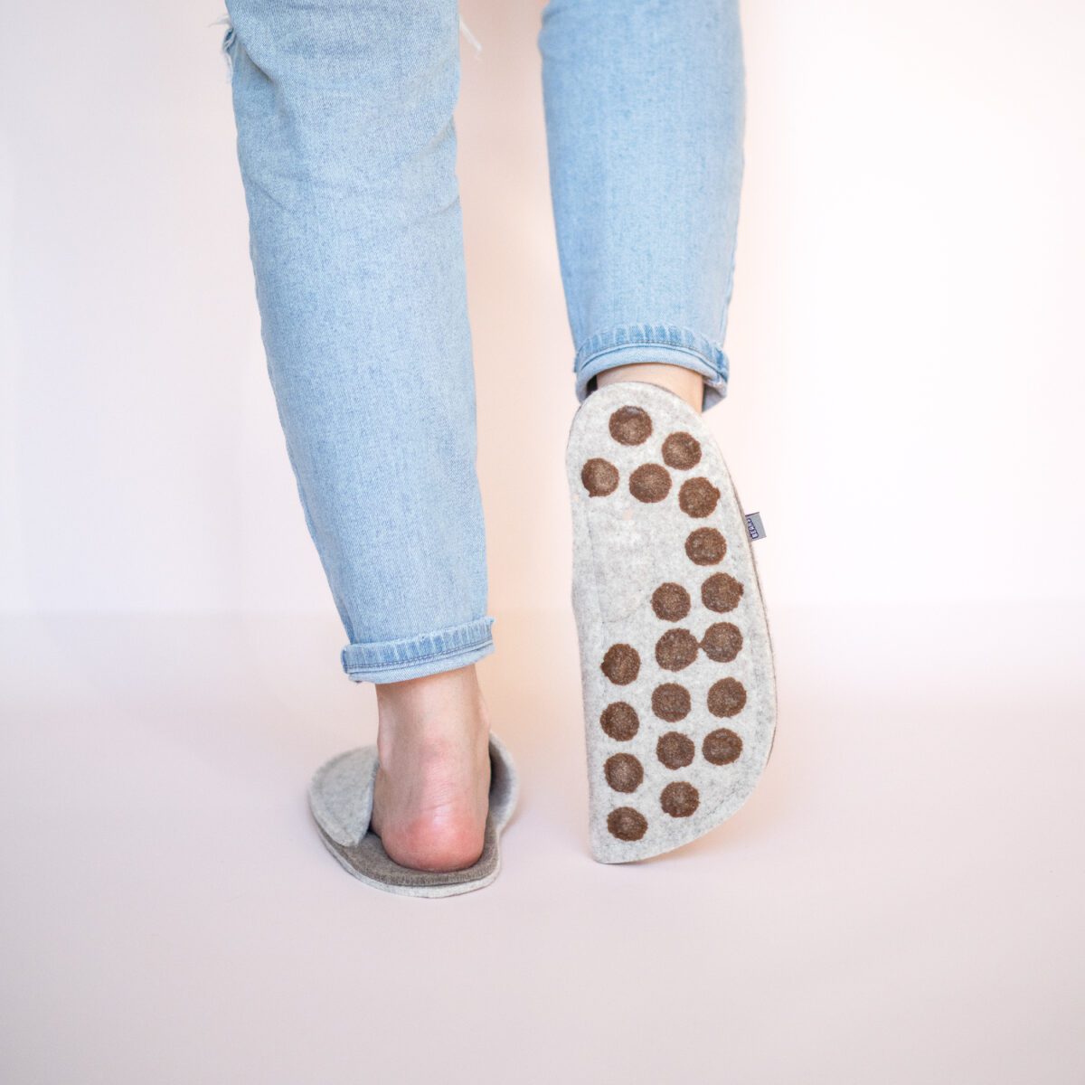 A woman wearing house slippers made of cream white and grayish brown wool felt