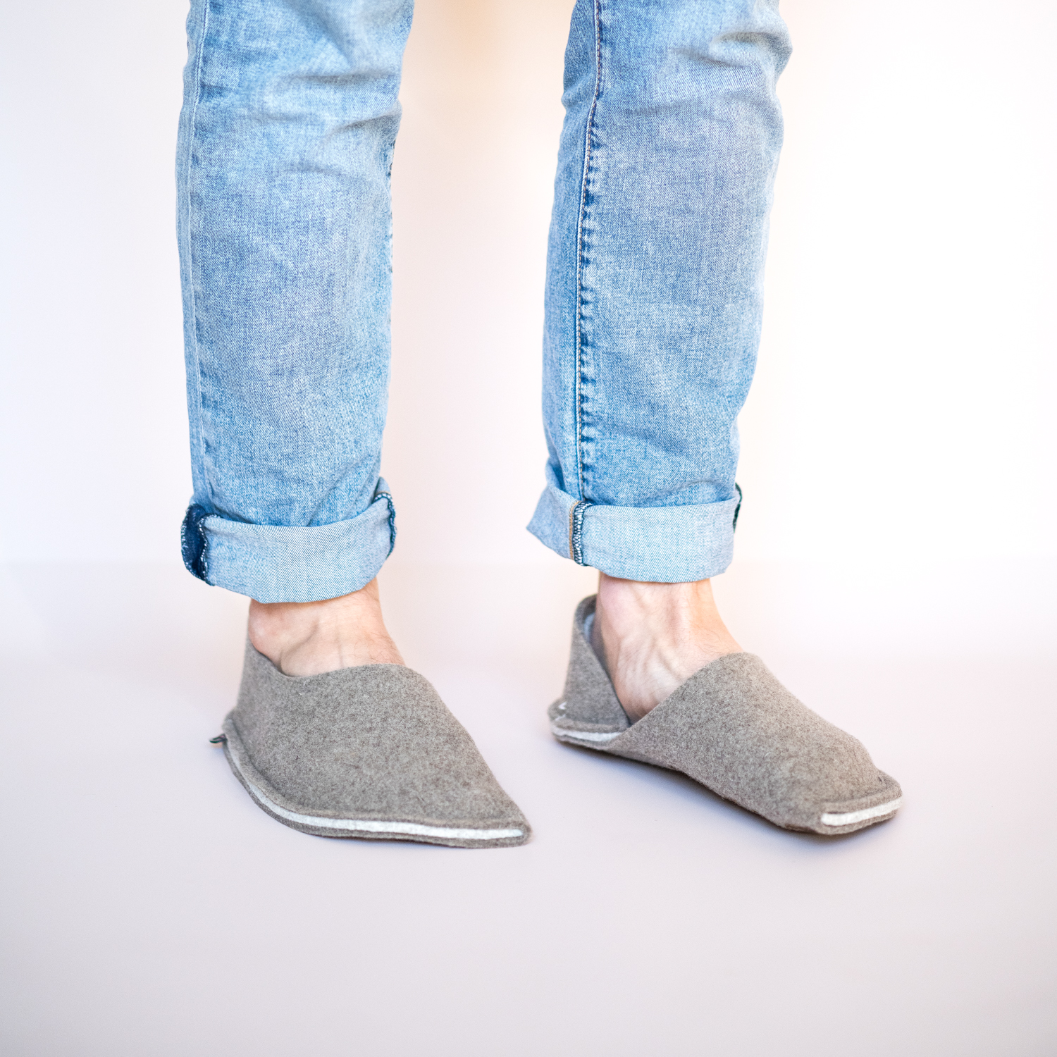 A man wearing house slippers made of grayish brown and cream white wool felt