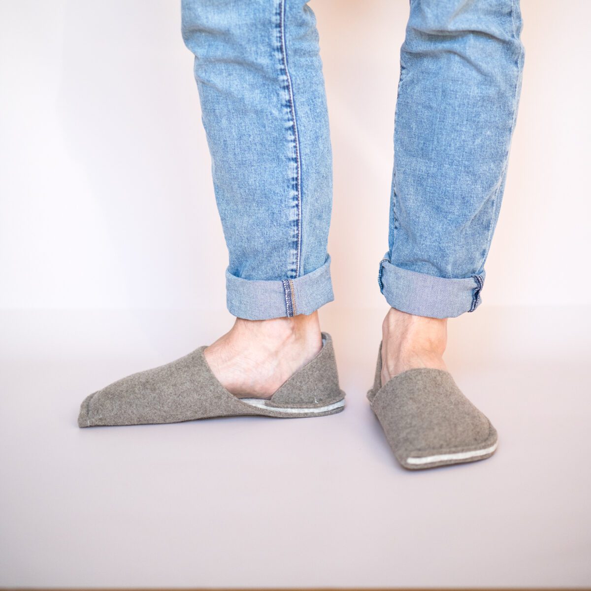 A man wearing house slippers made of grayish brown and cream white wool felt