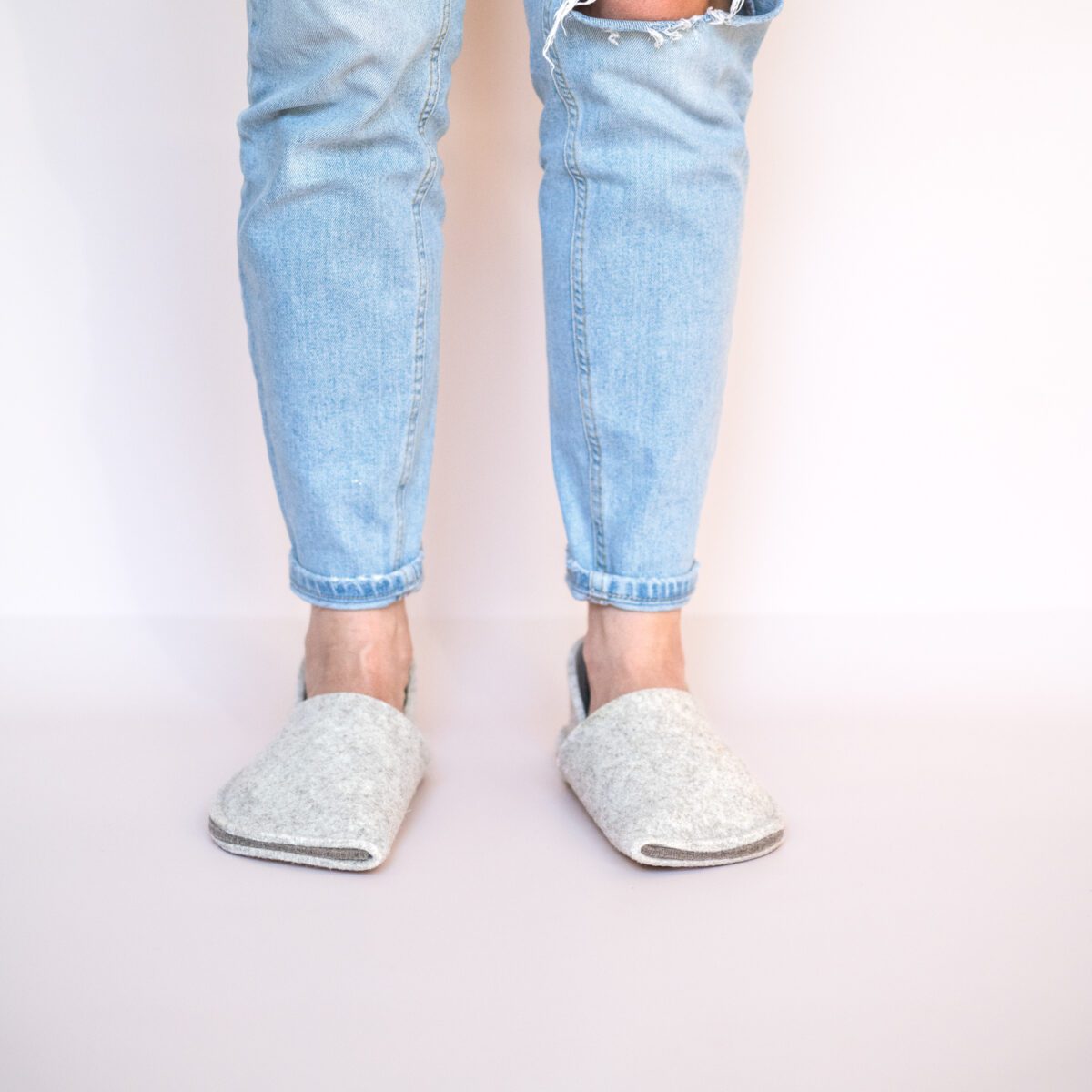 A woman wearing house slippers made of cream white and grayish brown wool felt