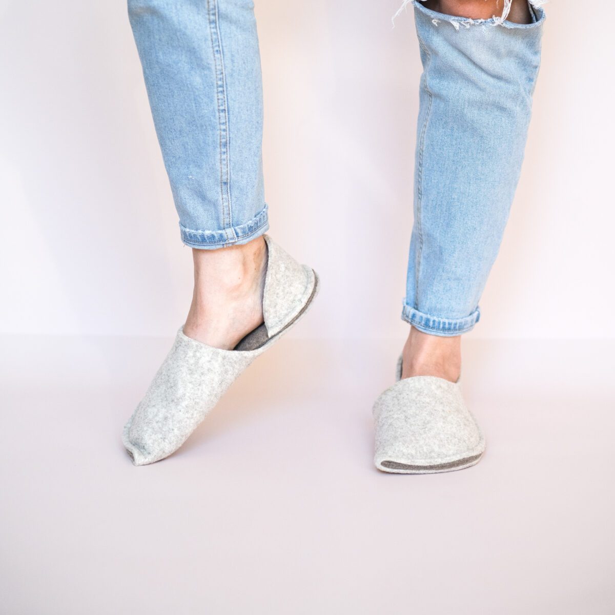 A woman wearing house slippers made of cream white and grayish brown wool felt