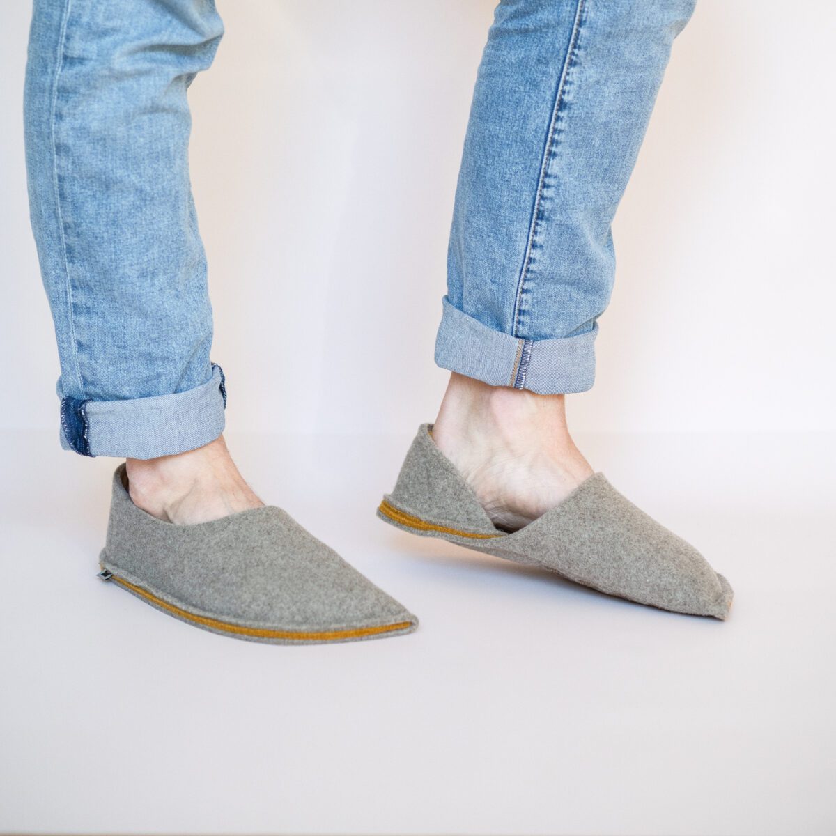 A man wearing house slippers made of grayish brown and curcuma yellow wool felt