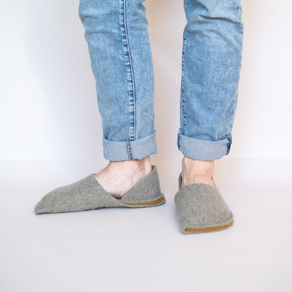 A man wearing house slippers made of grayish brown and curcuma yellow wool felt