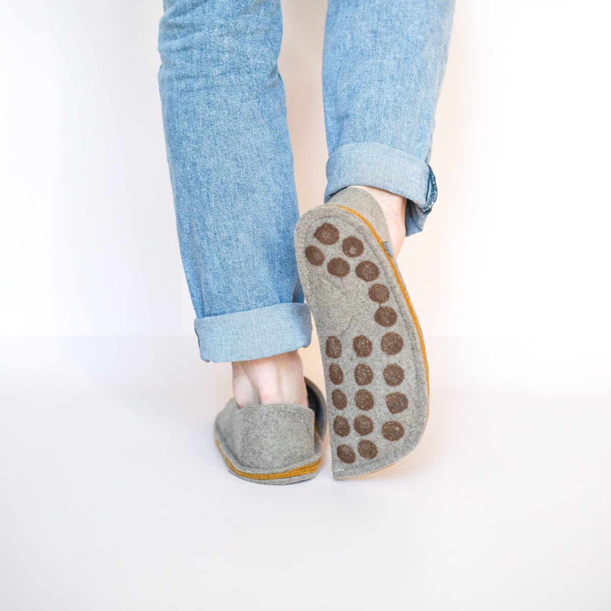 A man wearing house slippers made of grayish brown and curcuma yellow wool felt