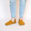 A woman wearing house slippers made of curcuma yellow and grayish brown wool felt