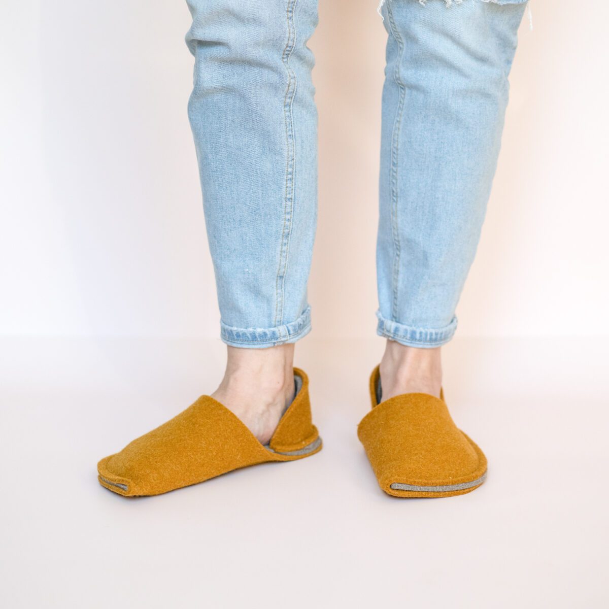 A woman wearing house slippers made of curcuma yellow and grayish brown wool felt