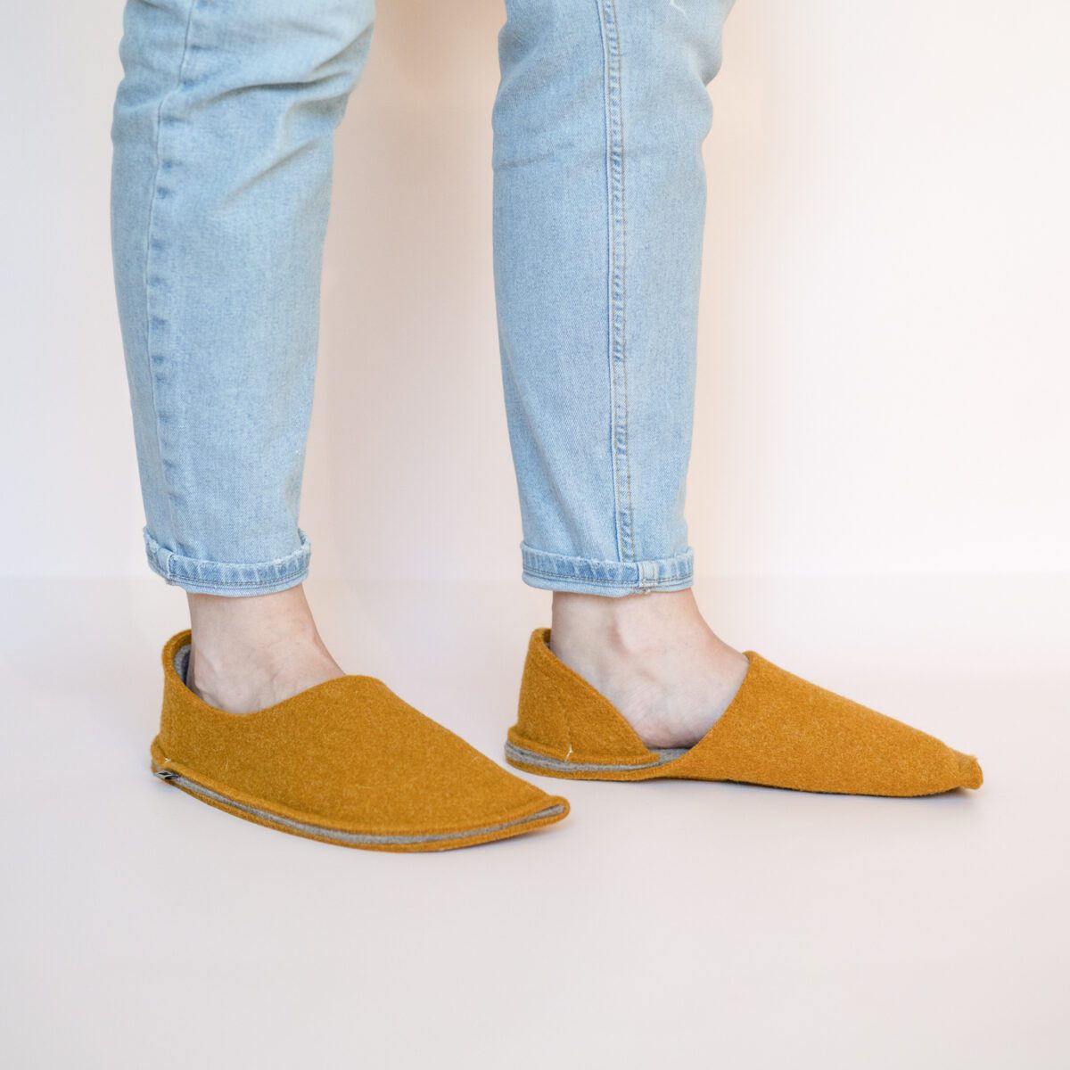 A woman wearing house slippers made of curcuma yellow and grayish brown wool felt