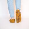 A woman wearing house slippers made of curcuma yellow and grayish brown wool felt