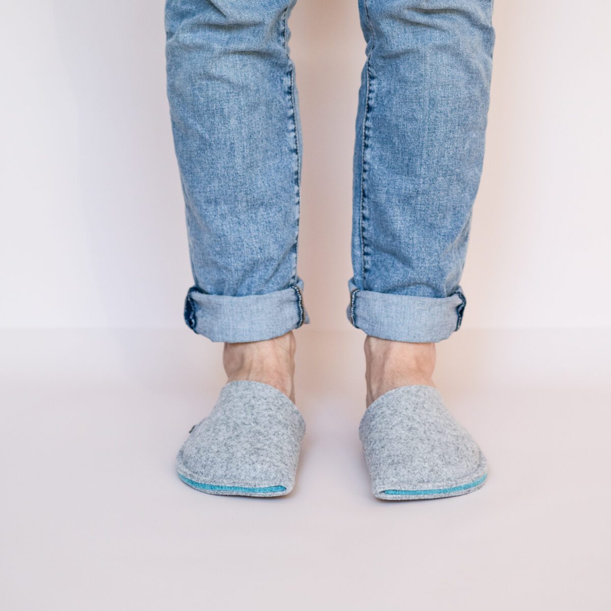 A man wearing slippers made of gray and blue wool felt.