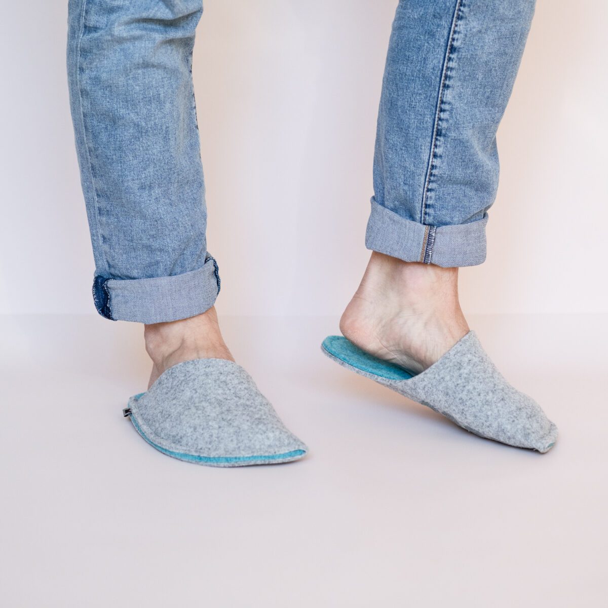 A man wearing slippers made of gray and blue wool felt.