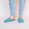 A woman wearing handmade house slippers made of turquoise blue and light gray wool felt slippers