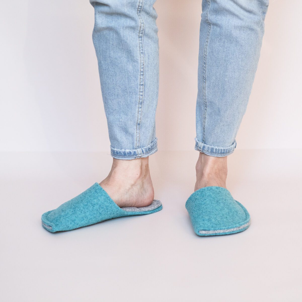 A woman wearing handmade house slippers made of turquoise blue and light gray wool felt slippers