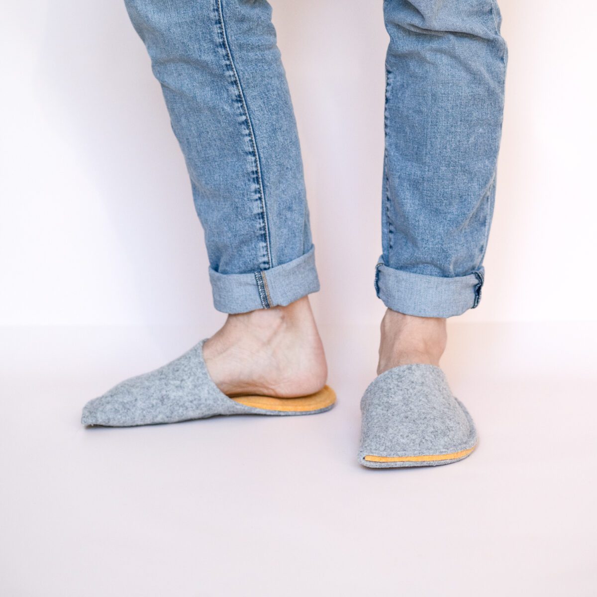 A man wearing house slippers made of light gray and peach yellow wool felt