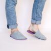 A man wearing house slippers made of light gray and purple wool felt