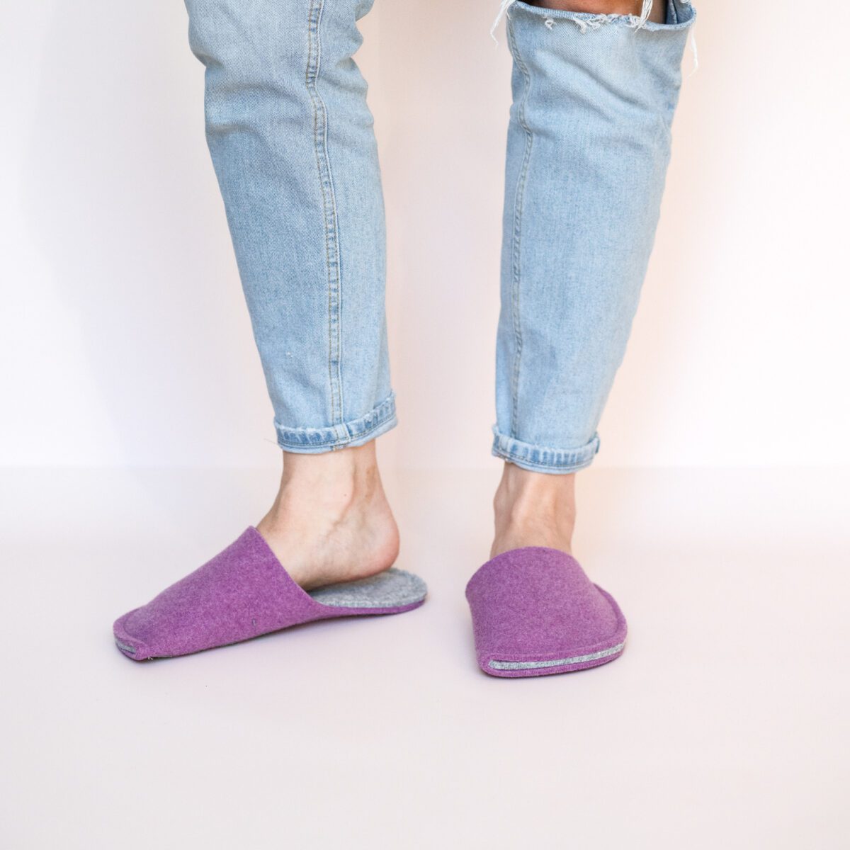 A woman wearing house slippers made of light gray and purple wool felt