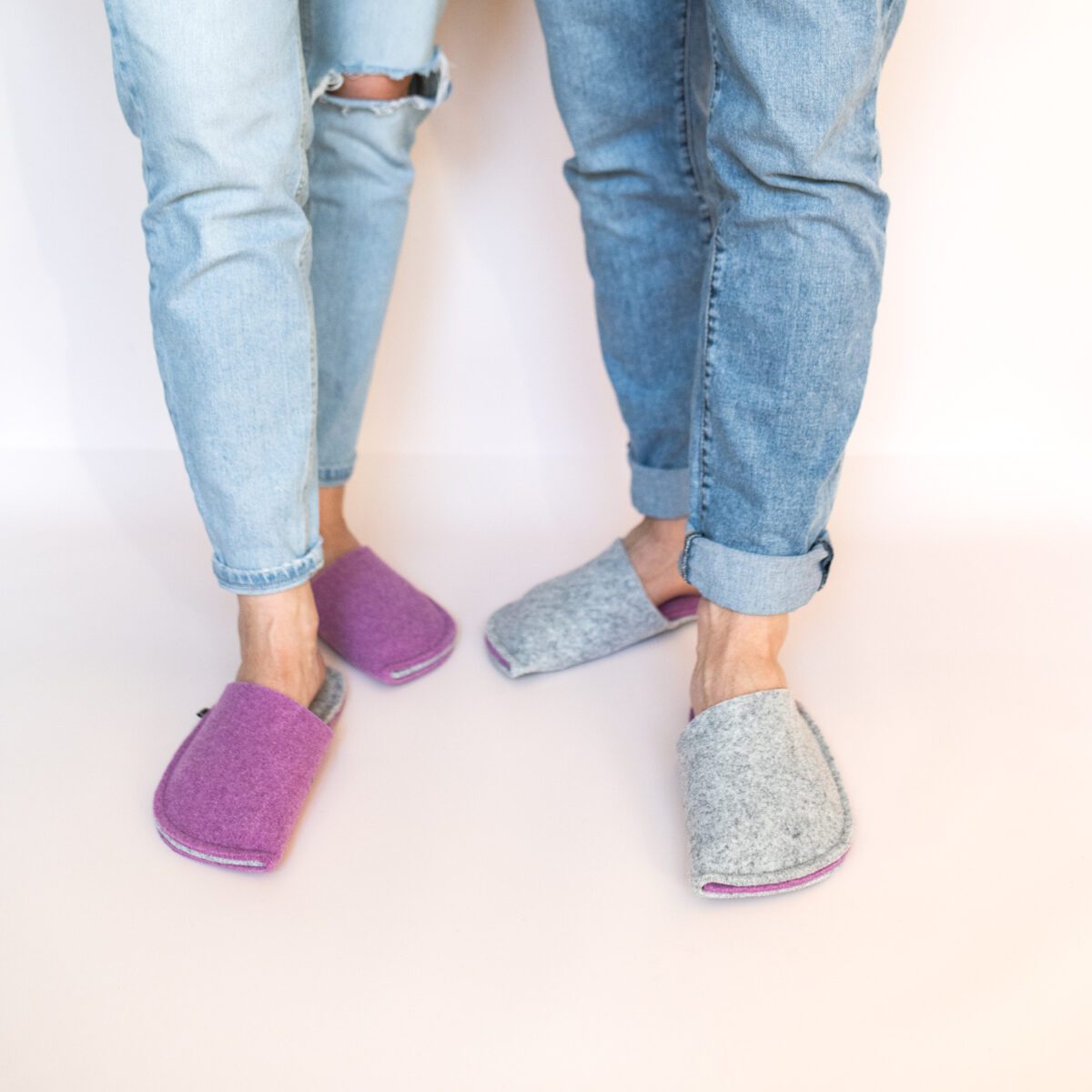 A man and a woman wearing house slippers made of light gray and purple wool felt