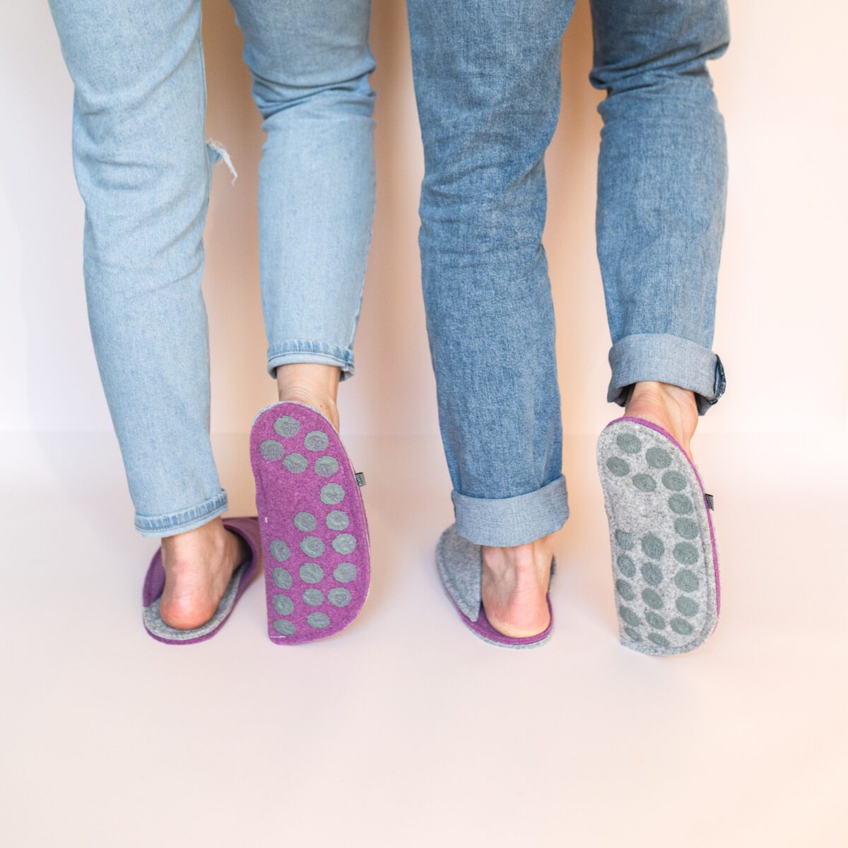 A man and a woman wearing house slippers made of light gray and purple wool felt