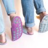 A man and a woman wearing house slippers made of light gray and purple wool felt