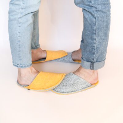 A man and a woman wearing house slippers made of light gray and peach yellow wool felt