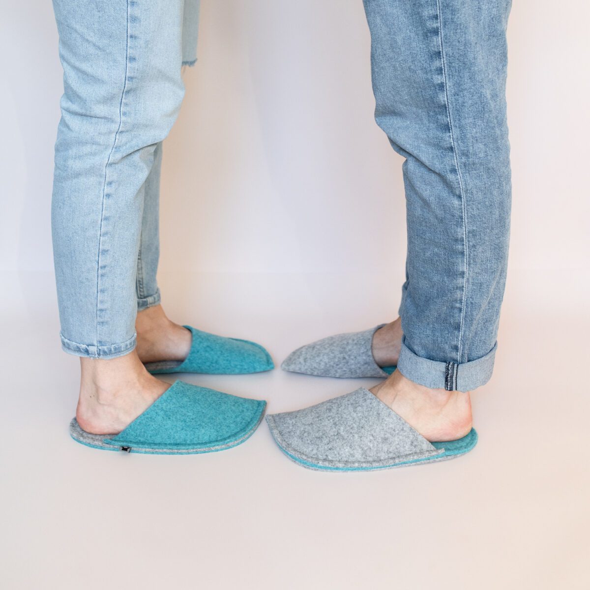 A man and a woman wearing slippers made of gray and blue wool felt.