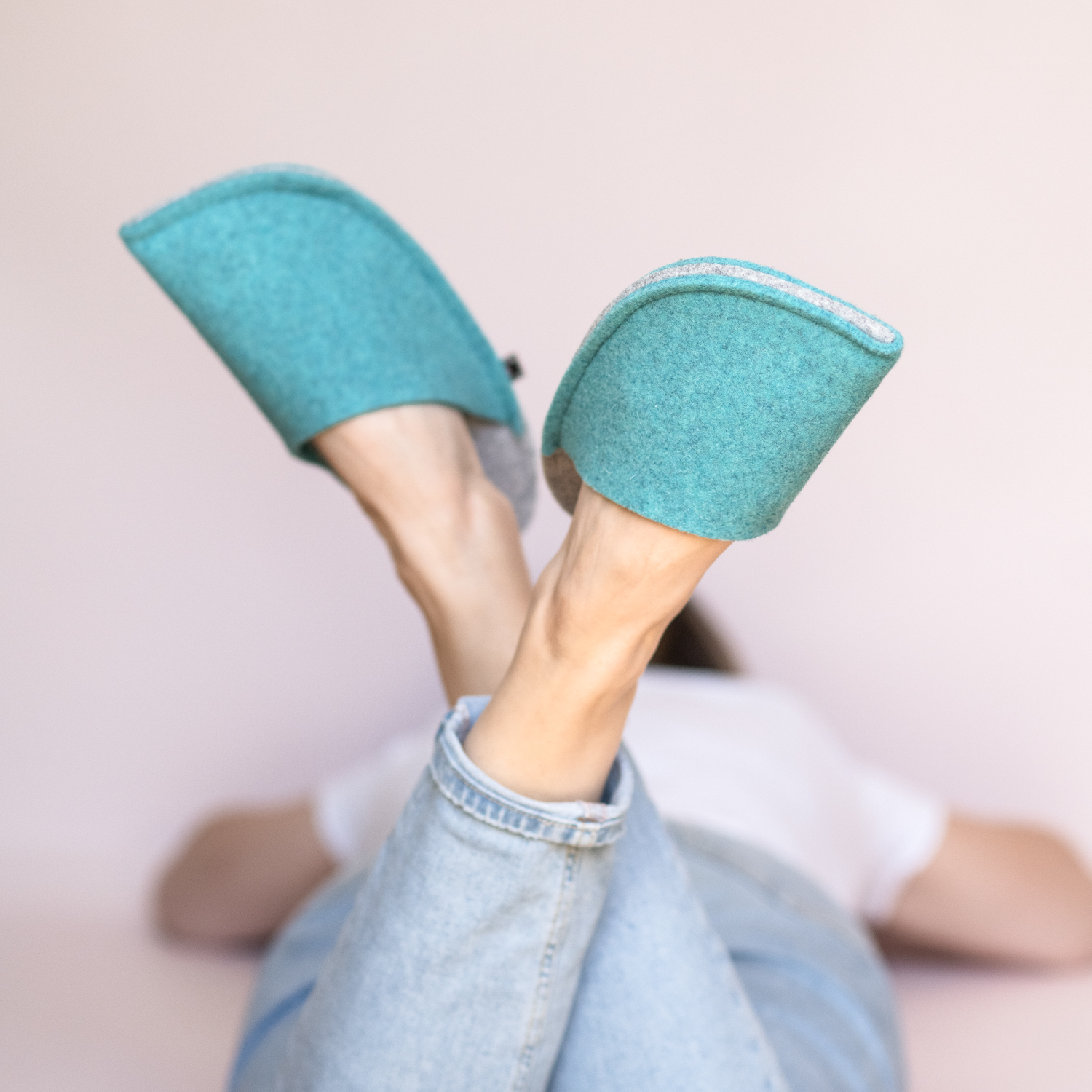 A woman wearing handmade house slippers made of turquoise blue and light gray wool felt slippers