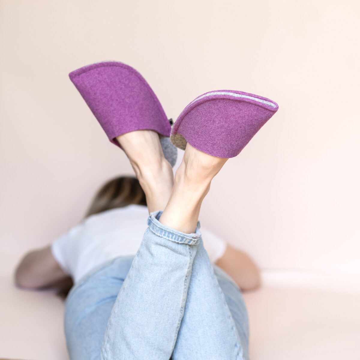 A woman wearing house slippers made of light gray and purple wool felt