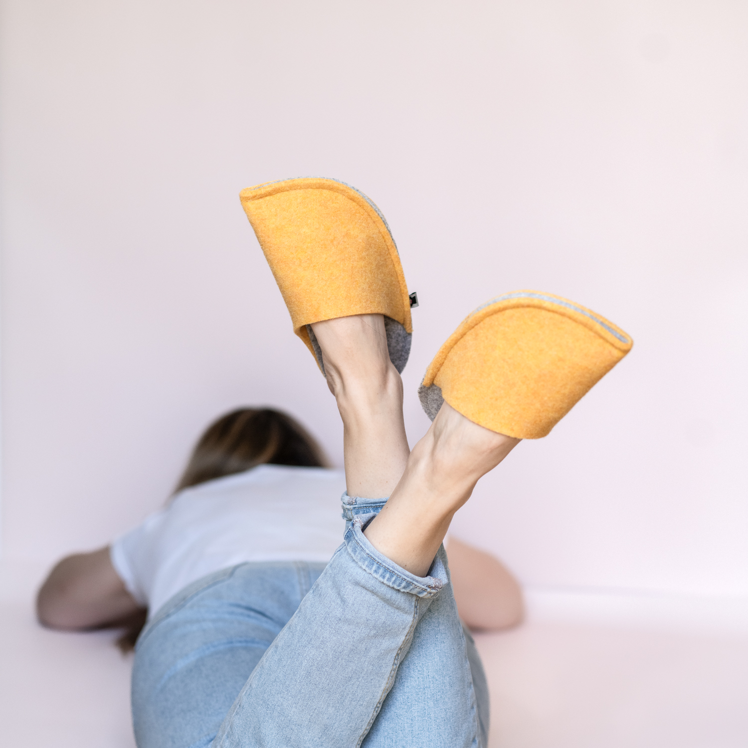 A woman wearing house slippers made of peach yellow and light gray wool felt