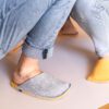 A man and a woman wearing house slippers made of light gray and peach yellow wool felt