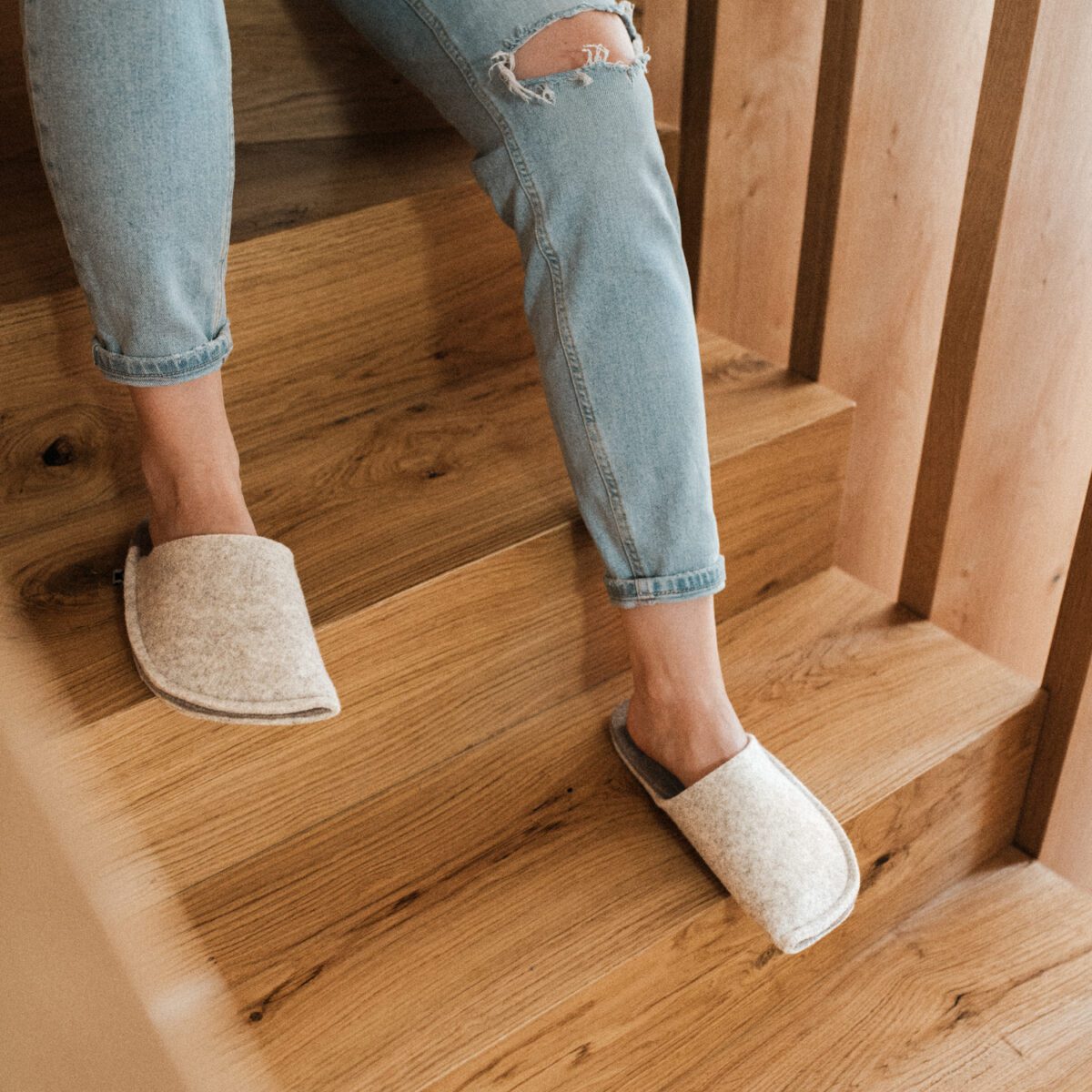 A woman wearing house slippers made of cream white and grayish brown wool felt