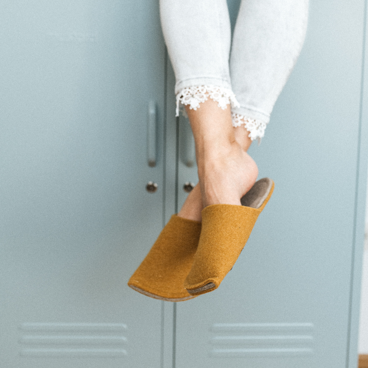 A woman wearing house slippers made of curcuma yellow and grayish brown wool felt