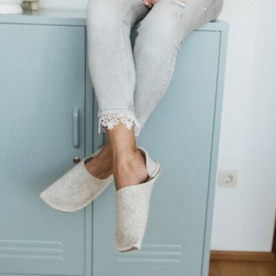 A woman wearing house slippers made of cream white and grayish brown wool felt